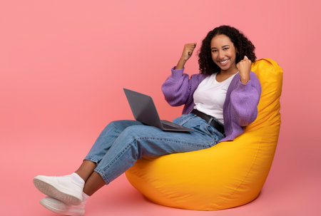 Young Woman Celebrates Victory While Winning Online Lottery in Pink Studio Settingの写真素材