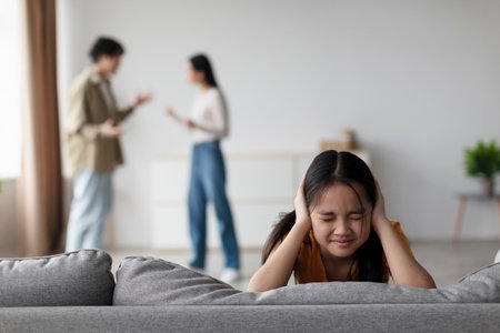 Emotional Girl Coping With Family Conflict While Parents Argue in a Modern Living Roomの写真素材