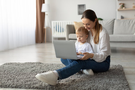 Mother and Toddler Enjoy Time Together While Working on a Laptop in a Cozy, Modern Living Roomの写真素材