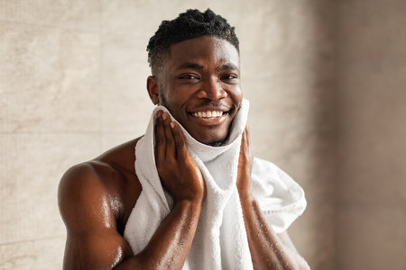 Joyful Black Man Smiling While Wiping Face With Towel in Bathroom After Morning Routineの写真素材
