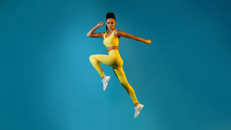Serious Female Athlete Jumps and Poses in Mid-Air Over a Blue Backgroundの写真素材