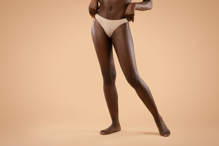 Long Slim Legs of an Unrecognizable Woman in Nude Underwear Against a Beige Backgroundの写真素材
