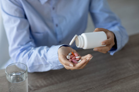 Young Indian Woman Pours Pills Into Her Hand at Home Workspace for Medication Managementの写真素材