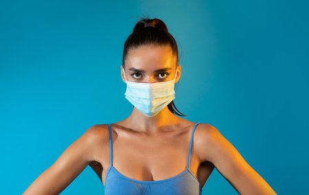 Sporty Lady in Face Mask Poses Confidently Against Blue Backgroundの写真素材