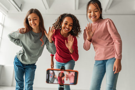 Three Diverse Girls Happily Waving at Smartphone While Creating a Fun Video Indoorsの写真素材