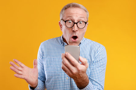 Mature Man Celebrates Exciting News Using Smartphone Against Bright Backgroundの写真素材