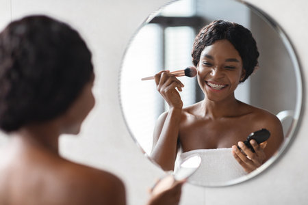 Beautiful Black Lady Applies Makeup in Bathroom Mirror During Morning Routineの写真素材