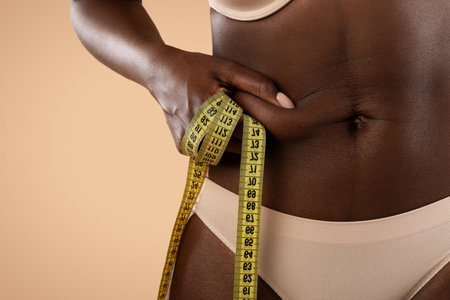 Black Woman Measuring Waist to Track Fitness Progress in Studio With Beige Backgroundの写真素材
