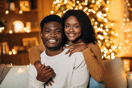 Millennial Black Couple Enjoying Holiday Warmth Together on Cozy Couch With Festive Lightsの写真素材