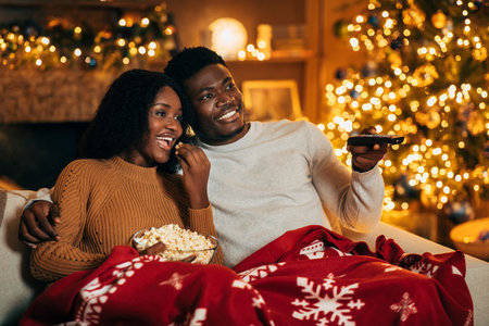 Black Couple Shares Joyful Christmas Eve Watching Movies and Enjoying Popcorn in Cozy Roomの写真素材