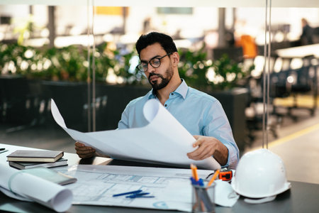 Man Reviewing Building Plans in a Modern Office Environment During the Dayの写真素材