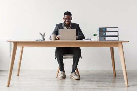 Cheerful African American Businessman Working on Laptop in Modern Office Settingの写真素材