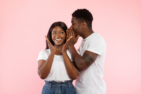 Couple Joyfully Sharing Exciting News While Whispering Secrets on Pink Backgroundの写真素材