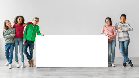 Diverse Group of Happy Kids Posing Together Near Blank Board in Gray Studio Settingの写真素材