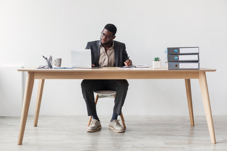 Serious African American Businessman Takes Notes During Online Training Session at Deskの写真素材