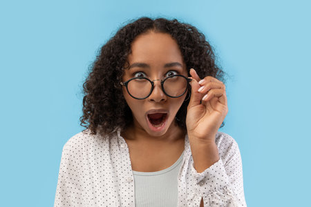 Emotional Black Female Student Surprised in Studio Against Blue Backgroundの写真素材
