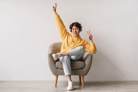 Funky Young Man Enjoys Music and Dancing in an Armchair Against a White Studio Wallの写真素材