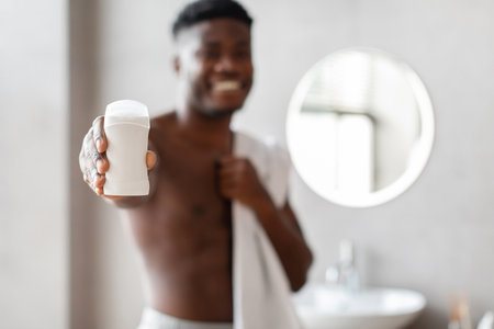African American Man Demonstrating Antiperspirant Stick in Modern Bathroom Settingの写真素材