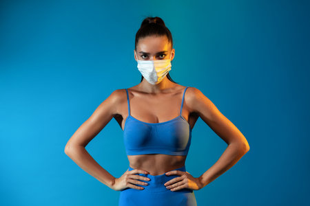 Sporty Lady Stands With Hands on Hips, Wearing a Protective Face Mask, Ready for a Workoutの写真素材