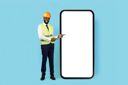 Construction Offer. Smiling Black Male Engineer Pointing At Huge Blank Smartphoneの写真素材