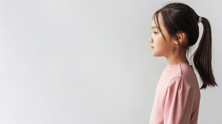 Profile Portrait of Serious Asian Preteen Girl in Pink Top on Gray Backgroundの写真素材