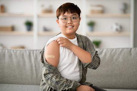 Korean Child Proudly Shows Vaccination Bandage While Sitting on Couch at Homeの写真素材