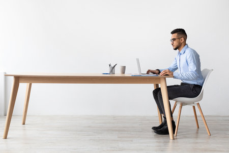 Focused Middle Eastern Manager Using Laptop in Modern Office Setting During Work Hoursの写真素材
