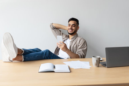 Relaxing Arab Man Enjoying Free Time at Home Office While Using Mobile Phoneの写真素材