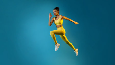 Young Lady Jumping in Mid-Air Over Blue Background in Yellow Sportswear