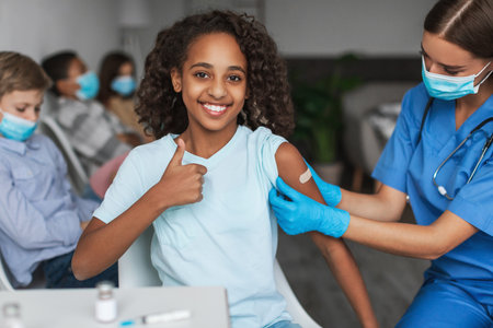 Cheerful Vaccinated Black Preteen Girl Giving Thumbs up After Getting Coronavirus Vaccine Indoorsの写真素材