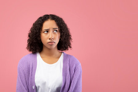 Thoughtful Young Black Woman in Pink Studio Background Showing Doubt and Reflectionの写真素材