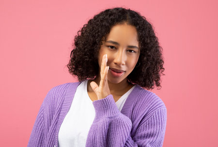Young Black Woman Sharing a Secret in a Pink Studio With a Playful Vibeの写真素材