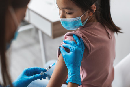 Nurse Administers Covid-19 Vaccination to Young Korean Girl in Clinic Settingの写真素材