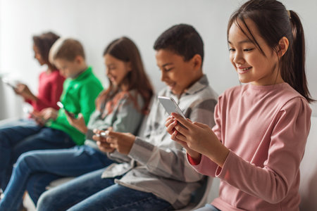 Diverse Children Engaged in Mobile Gaming and Online Activities Against a Gray Backgroundの写真素材