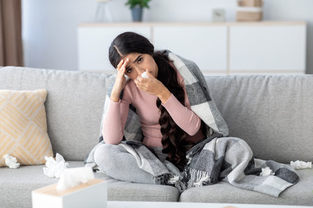 Frustrated Millennial Indian Woman With Cold Symptoms Seeks Comfort on Sofa at Homeの写真素材