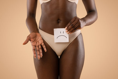 Black Woman Expressing Sadness About Health Issues in Beige Studio Settingの写真素材