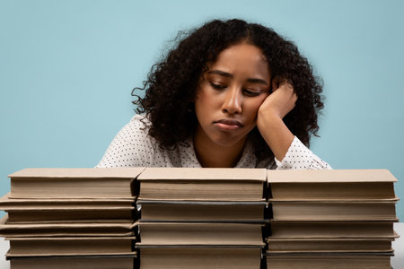 Exhausted Young Woman Studying for Exam With Stacks of Books in Blue Backgroundの写真素材