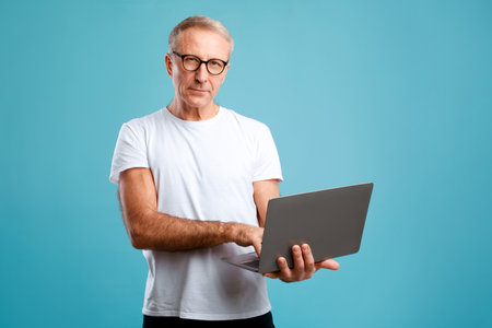 Confident Mature Man Using Laptop in Blue Studio Background