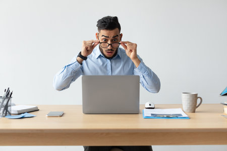 Confused Man Reacts to Unexpected News While Working on Laptop at Deskの写真素材