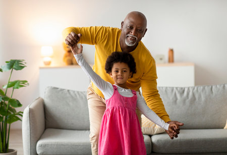 Smiling Little Girl and Grandfather Dancing in Living Room During Joyful Family Time Togetherの写真素材