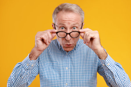 Surprised Mature Man Expresses Shock at Unexpected News Against Bright Yellow Backgroundの写真素材