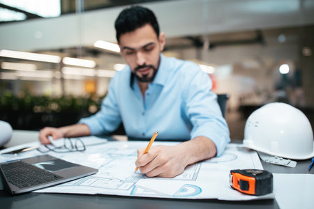 Professional Man Working on Architectural Plans at a Modern Office With Construction Tools Around Himの写真素材