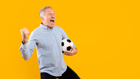 Mature Man Celebrates Soccer Victory With Joyful Scream and Soccer Ball on Yellow Backgroundの写真素材