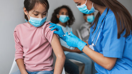 Nurse Administers Covid-19 Vaccine to Young Girl Indoors in Modern Clinic Settingの写真素材