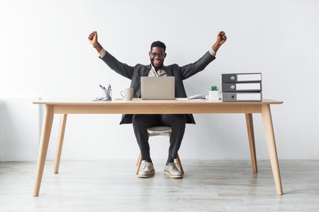 Excited Young Black Businessman Celebrating Success While Sitting at Desk With Laptopの写真素材