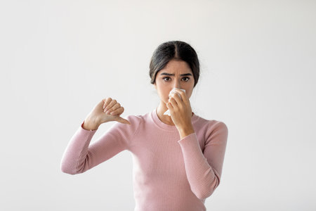 Young Indian Lady Sneezes in Napkin While Feeling Unwell and Shows Thumb Down