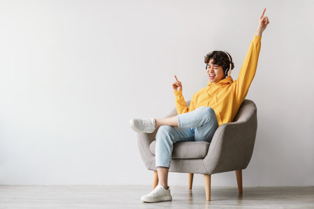 Joyful Young Man Dancing in Armchair While Listening to Music in a Bright Roomの写真素材