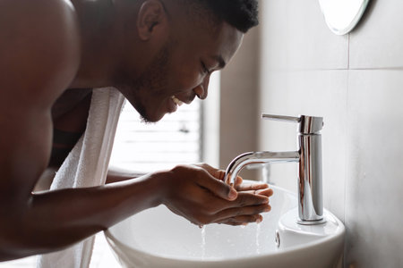 Young Black Man Performing Morning Hygiene Routine in Modern Bathroomの写真素材