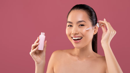 Korean Lady Enjoys Nourishing Serum With Radiant Smile in Vibrant Studio Settingの写真素材