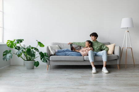 Young Couple Enjoys Remote Communication on Laptop While Relaxing at Home Togetherの写真素材